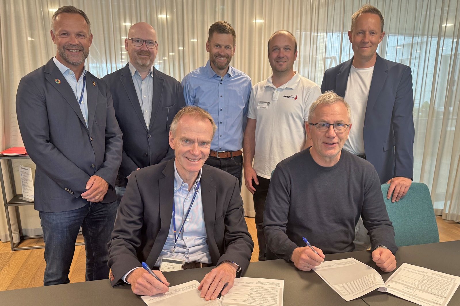 De to som signerer kontraktene sitter foran, mens de andre står i en halvsirkel bak.