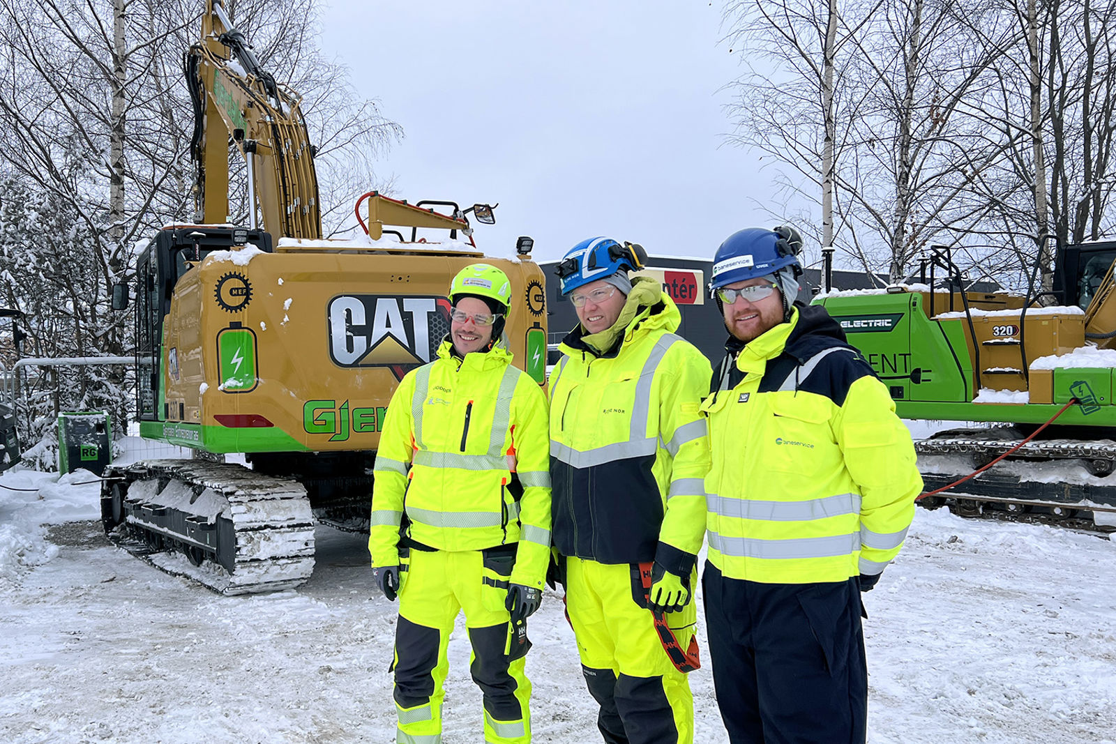 Personene i anleggsutstyr foran to gravemaskiner tilkoblet ladekabler.
