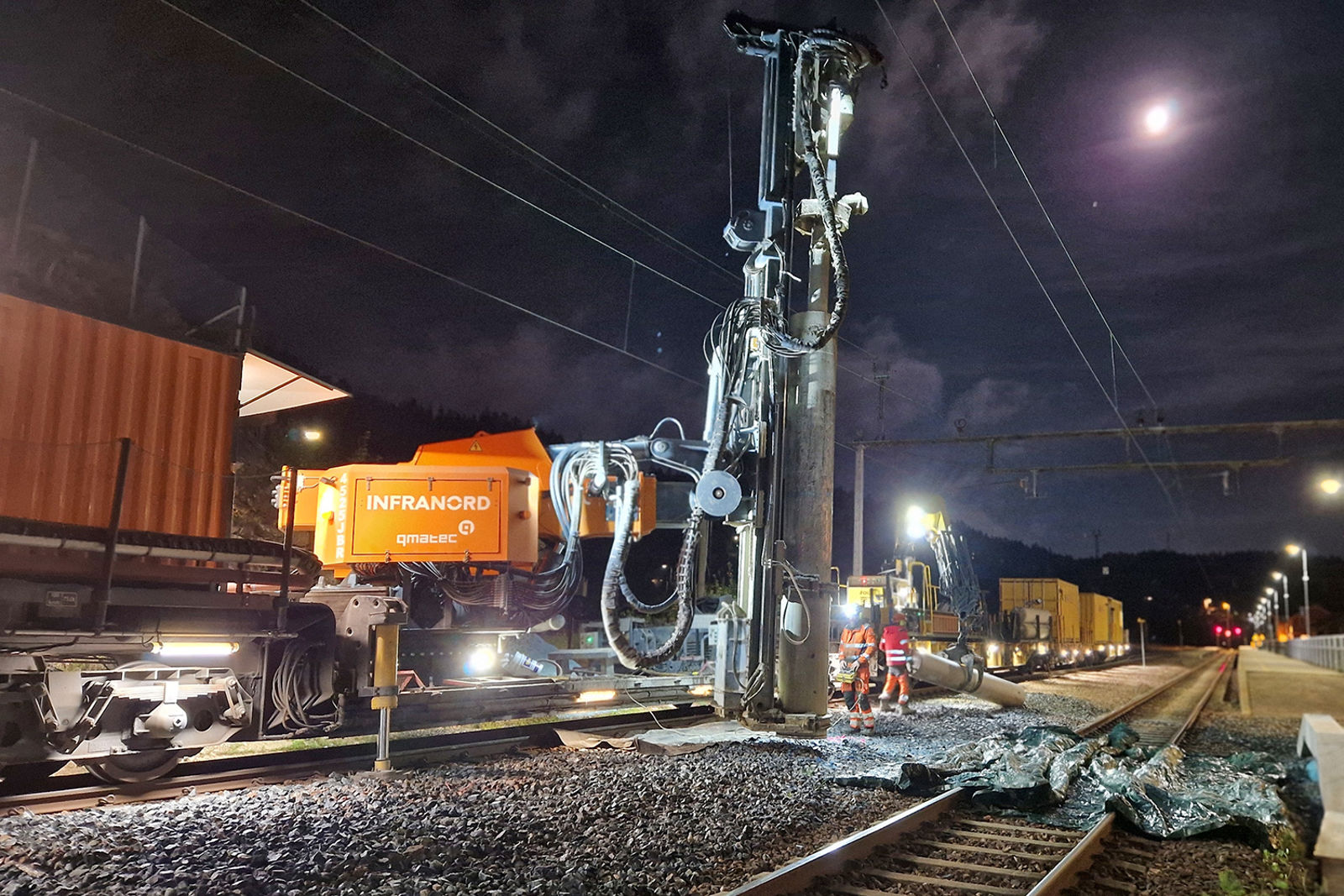 Boring pågår mellom to spor på en stasjon med et stort spesialtog. Det er natt og måneskinn.