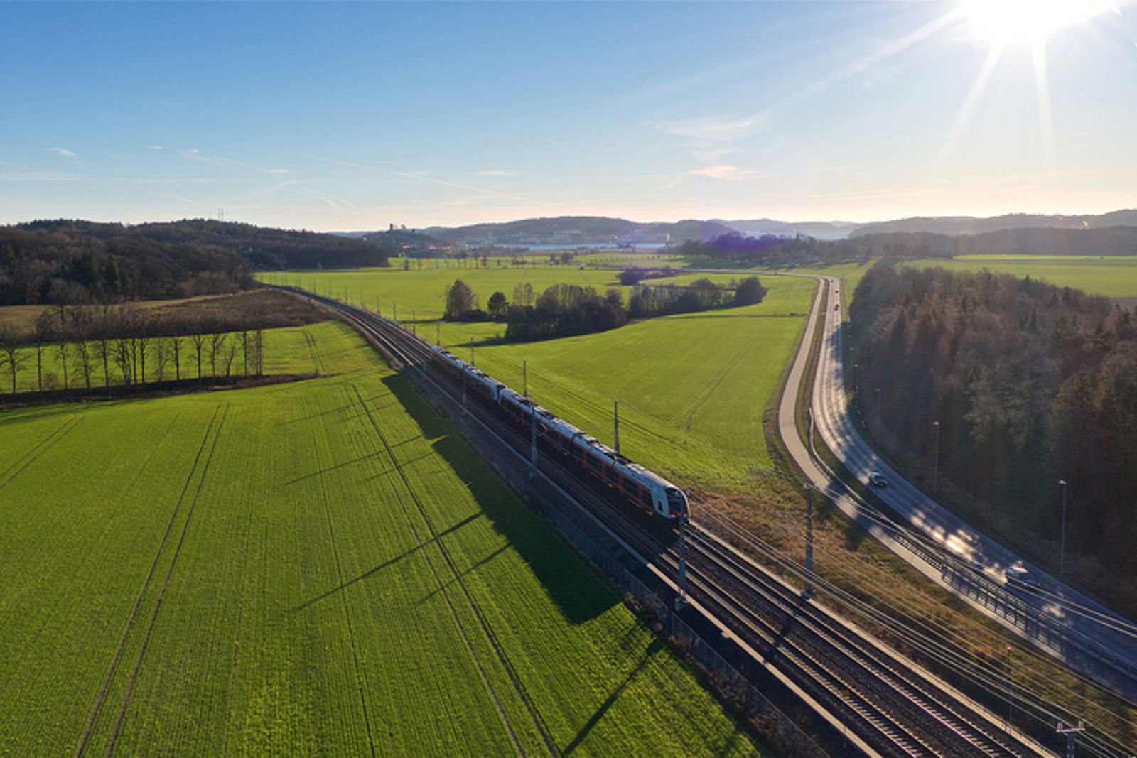 Tog på spor med grønne jorder på hver sin side