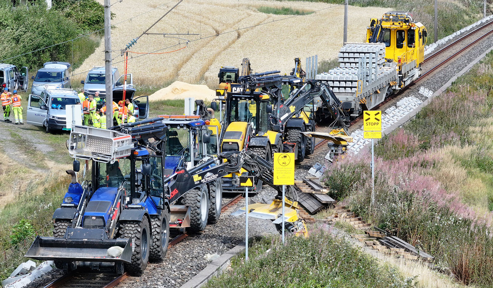 Skinnetraktorer og maskiner står parkert i sporet, mens en gruppe arbeidere står ved siden av.