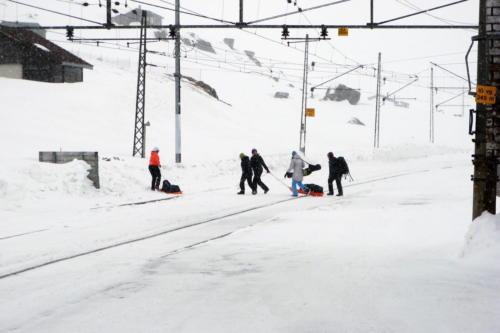 Folk som går over jernbanesporet, bærende på sekker, akebrett og ski, på Finse stasjon.
