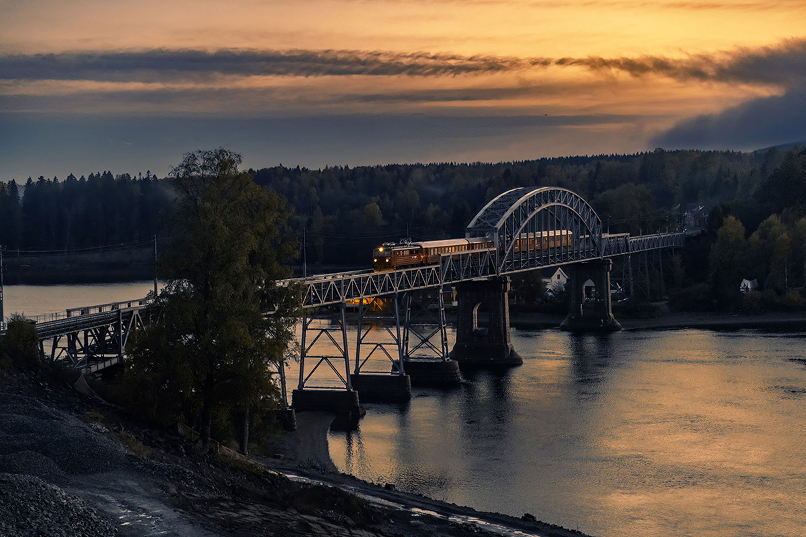 Et gammelt, elektrisk togsett er ute på brua i skumringstimen.