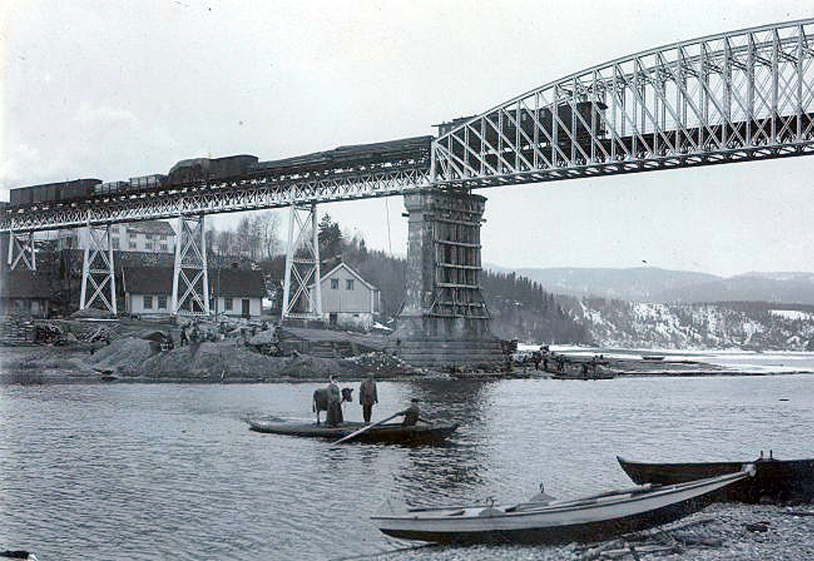 Robåten midt ute i elva ved siden av brupillaren, et tog oppe på brua.