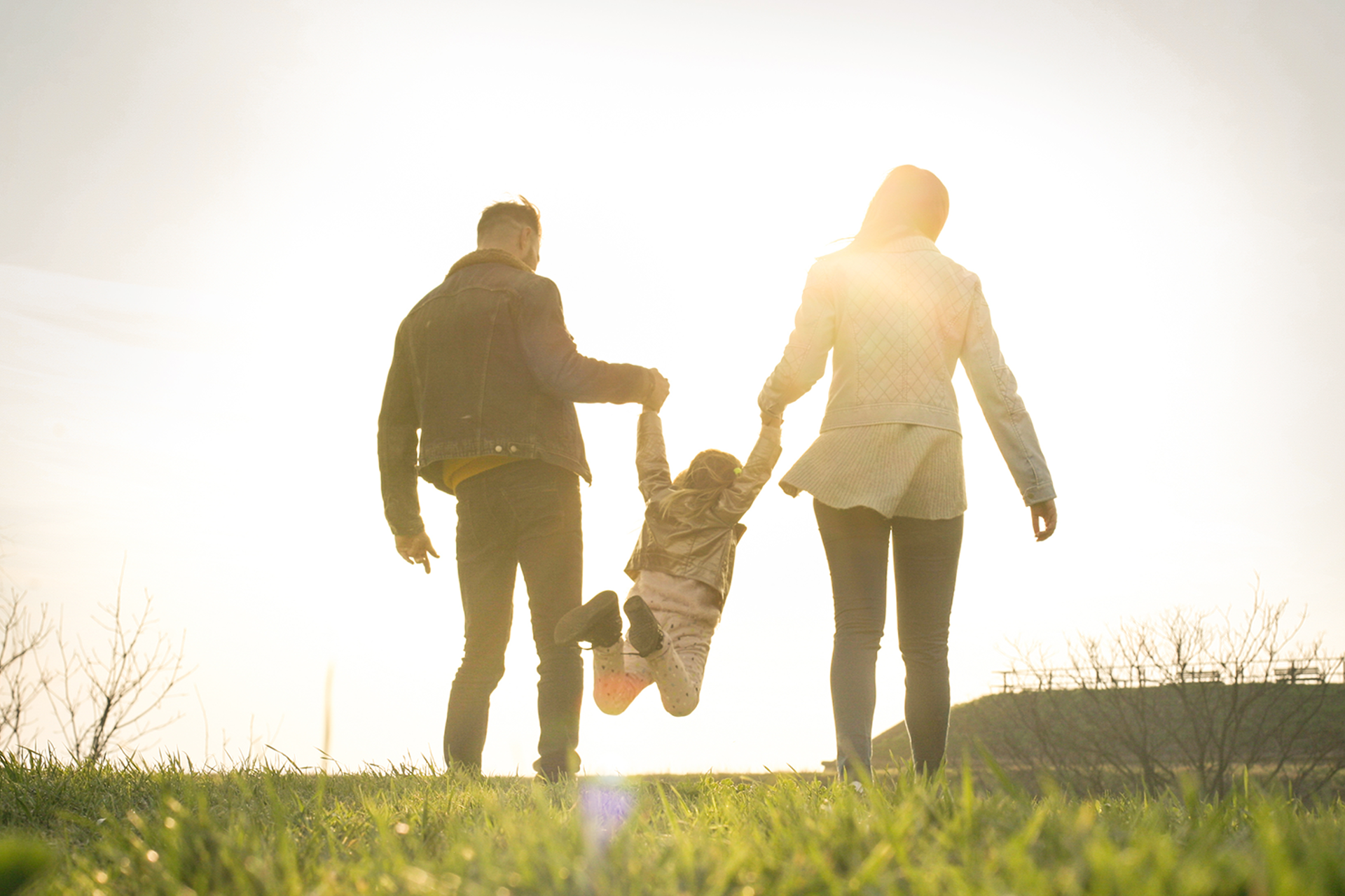 Mann og dame løfter barn i hendene i solnedgangen